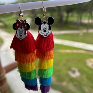 May include: Rainbow tassel earrings with Mickey Mouse and Minnie Mouse character charms. The charms are silver with black outlines and red accents. The tassels are layered in red, orange, yellow, green, blue, and purple.