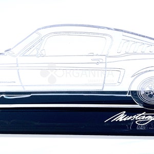 May include: A clear acrylic model of a classic Ford Mustang car on a black base. The model is a side profile of the car and includes the word "Mustang" in cursive on the base.