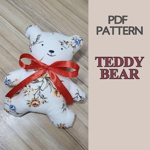 May include: A stuffed teddy bear made of white fabric with a floral pattern featuring orange and blue flowers, accented by a bright red satin ribbon tied in a bow around its neck. The text PDF PATTERN TEDDY BEAR is printed on the right side.