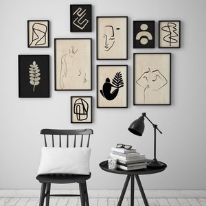 May include: A black chair with a white pillow sits in front of a white wall with black framed artwork. A black side table with a lamp and a stack of books sits next to the chair.