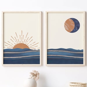 May include: Two framed prints with abstract minimalist designs. The left print features a stylized sun rising over a blue and white striped horizon. The right print features a stylized moon with a blue and brown marbled design over a blue and white striped horizon.