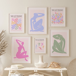 Op de afbeelding: Vijf ingelijste prints van Matisse-kunstwerken met een kleurenschema in roze, blauw, groen en oranje. De prints hangen aan een witte muur boven een witte bank met twee witte rieten manden. De bank staat op een wit tapijt met een zwart geometrisch patroon.