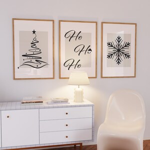 May include: Three framed prints with a Christmas theme. The left print features a stylized black Christmas tree with stars. The middle print has the text "Ho Ho Ho" in black cursive. The right print features a black snowflake.