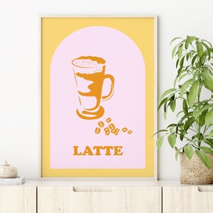 May include: A yellow and pink poster with a graphic of a latte in a glass with coffee beans scattered around it. The text "LATTE" is printed in orange below the graphic.