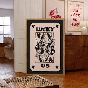 Pu&ograve; includere: Illustrazione in bianco e nero di una carta da gioco della regina di cuori con le parole "Lucky Us" su uno sfondo rosa.