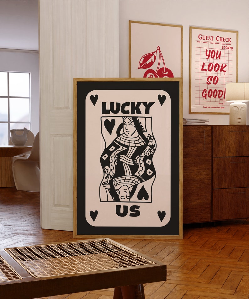 Pu&ograve; includere: Illustrazione in bianco e nero di una carta da gioco della regina di cuori con le parole "Lucky Us" su uno sfondo rosa.