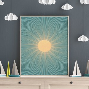 May include: A framed print of a stylized sun with radiating lines in shades of yellow and teal against a blue background.