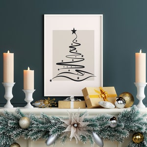 May include: A white mantelpiece decorated with a green garland, gold and silver ornaments, and two white candle holders with lit candles. A framed print of a black abstract Christmas tree design hangs above the mantel.