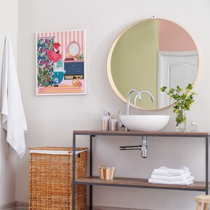May include: A bathroom vanity with a white porcelain sink and a round mirror with a gold frame. The vanity has a wooden top and a black metal frame. There is a wicker laundry basket on the left side of the vanity.