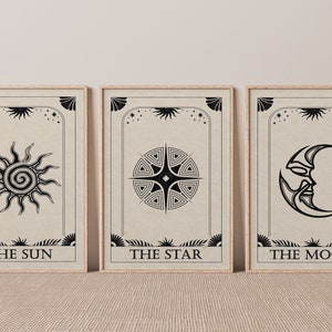May include: Three framed prints with black and white illustrations of the sun, star, and moon. The prints have a beige background and the text "THE SUN", "THE STAR", and "THE MOON" at the bottom.