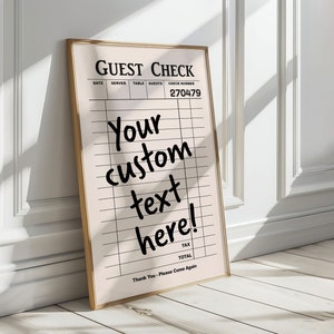 May include: A gold framed sign with a white background and black text that reads "GUEST CHECK". The sign has columns for date, server, table, guests, and check number. The check number is 270479. The sign also has a section for tax and total. The text "Your custom text here!" is written in black marker on the sign.