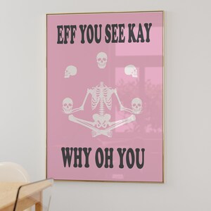 May include: A framed pink poster with the text "EFF YOU SEE KAY WHY OH YOU" in black. The poster features a white skeleton in a seated yoga pose, surrounded by white skulls. The frame is gold.