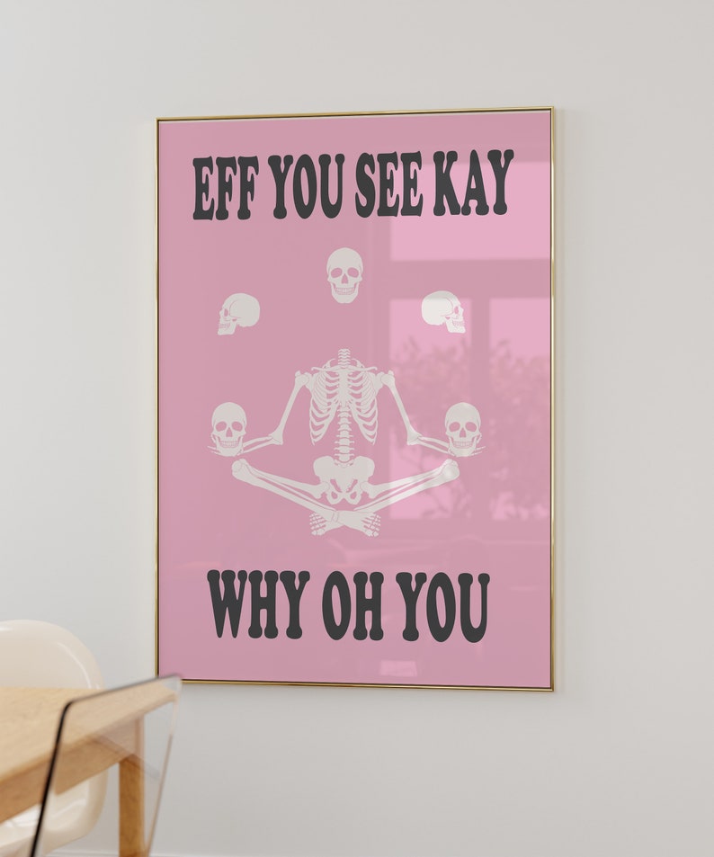 May include: A framed pink poster with the text "EFF YOU SEE KAY WHY OH YOU" in black. The poster features a white skeleton in a seated yoga pose, surrounded by white skulls. The frame is gold.
