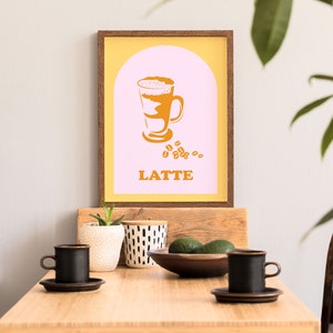 May include: A framed print with a yellow background and a pink arch. The arch contains a graphic of a latte in a glass with the word "LATTE" below it.