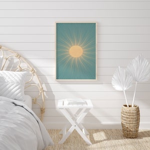 May include: A white bedroom with a white bed with a woven headboard, a white side table, a white framed print of a sun with teal rays, and a woven basket with white palm leaves.
