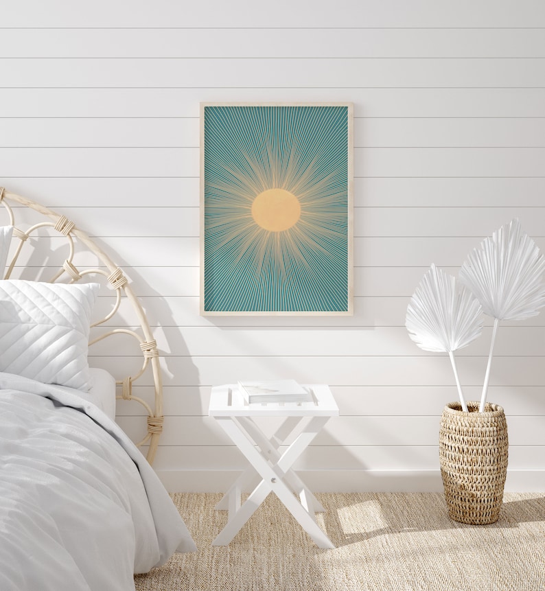 May include: A white bedroom with a white bed with a woven headboard, a white side table, a white framed print of a sun with teal rays, and a woven basket with white palm leaves.