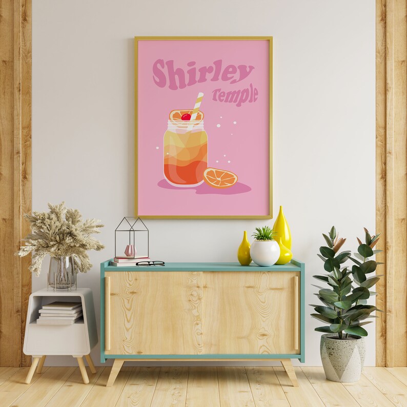 May include: A pink poster with a gold frame featuring a glass jar with a Shirley Temple cocktail. The text "Shirley Temple" is in a retro font.