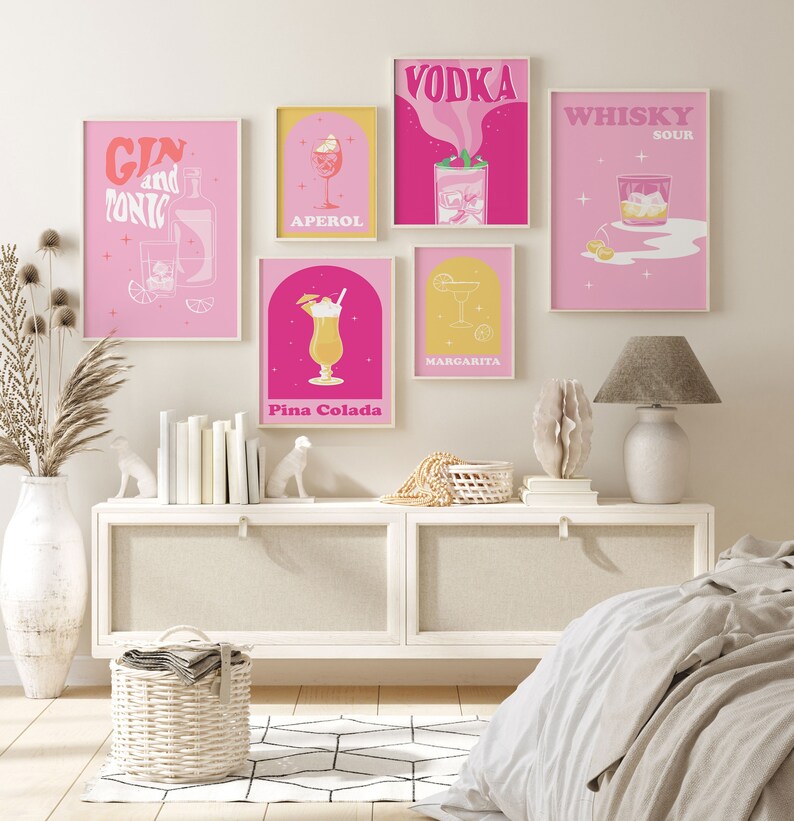 Puede incluir: Cinco impresiones ilustradas de c&oacute;cteles rosas y amarillas con los nombres "Gin and Tonic", "Aperol", "Vodka", "Margarita" y "Whiskey Sour". Las impresiones est&aacute;n enmarcadas y colgadas en una pared blanca sobre una c&oacute;moda blanca con una l&aacute;mpara blanca y una cesta de mimbre.