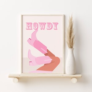 Pu&ograve; includere: Una stampa d'arte da parete stampabile rosa e bianca con la parola "HOWDY" in un font vintage. La stampa presenta un paio di stivali da cowboy rosa con una gamba abbronzata.