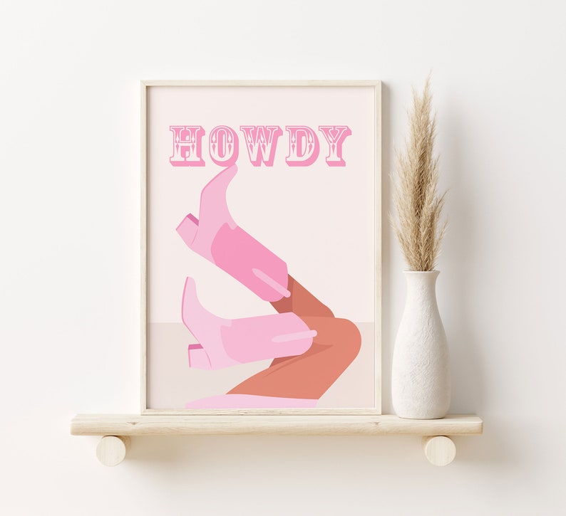 Pu&ograve; includere: Una stampa d'arte da parete stampabile rosa e bianca con la parola "HOWDY" in un font vintage. La stampa presenta un paio di stivali da cowboy rosa con una gamba abbronzata.