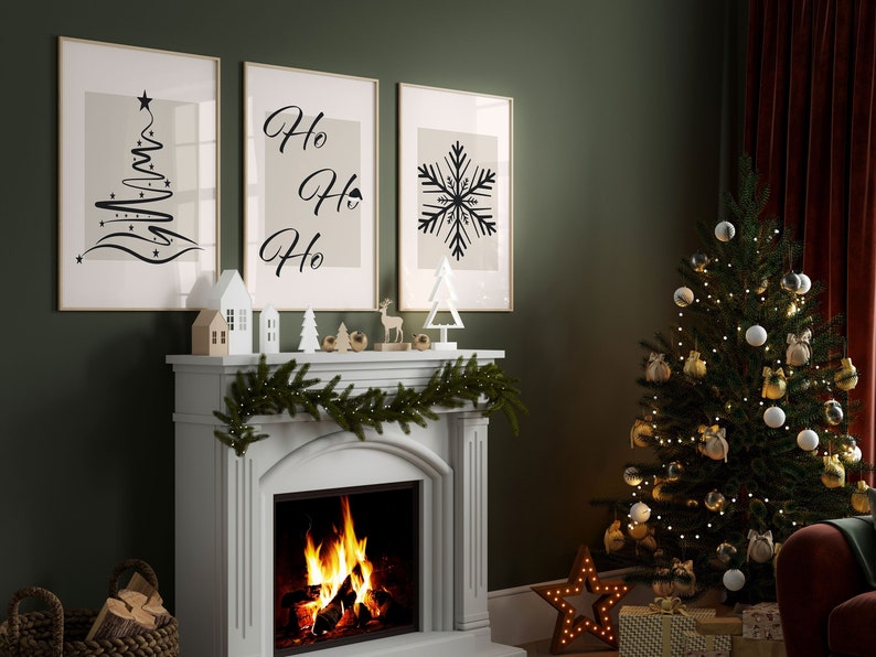 May include: A white fireplace mantel with a green garland and a lit fireplace. Three framed prints hang above the mantel, one with a stylized Christmas tree, one with the text "Ho Ho Ho", and one with a snowflake. A small Christmas tree with white and gold ornaments sits in the corner of the room.