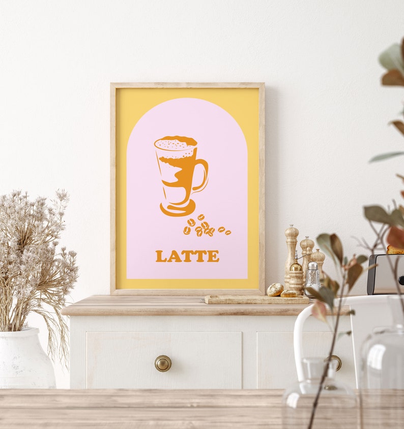 May include: A printable poster with a yellow frame and a pink background. The poster features a stylized illustration of a latte in a glass with a brown and white design. The text "LATTE" is printed in orange below the illustration.