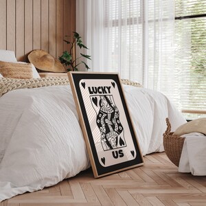 Pu&ograve; includere: Poster in bianco e nero con un design di carta da gioco della regina di cuori. La carta dice "LUCKY US" con cuori attorno ai bordi.