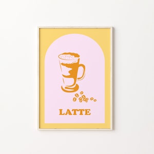 May include: A framed print with a yellow and pink background. The print features a stylized illustration of a latte in a glass with a brown and white design. The word "LATTE" is printed in orange below the illustration.