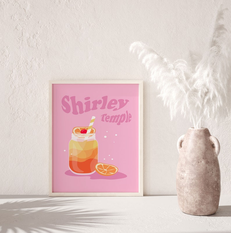 May include: A pink printable poster with the text "Shirley Temple" in a retro font. The poster features a cartoon illustration of a glass jar with a yellow and orange drink, a cherry, and a straw. A slice of orange is next to the jar.