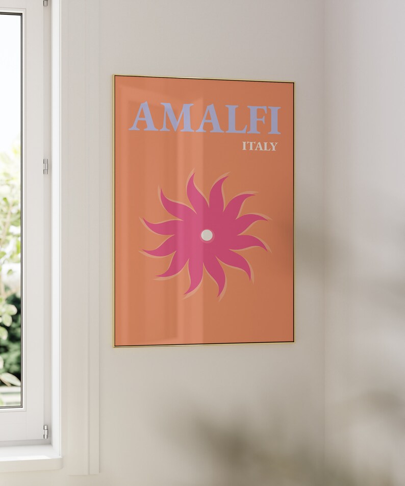 K&ouml;nnte beinhalten: Ein gerahmter Druck mit einem pfirsichfarbenen Hintergrund und einer stilisierten rosa Blume mit wei&szlig;em Zentrum. Der Text "AMALFI ITALIEN" ist in hellblau gedruckt.