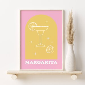Puede incluir: Una impresi&oacute;n de arte de pared imprimible rosa y amarilla con un contorno blanco de un vaso de margarita y rodajas de lima. El texto "MARGARITA" est&aacute; en la parte inferior de la impresi&oacute;n.