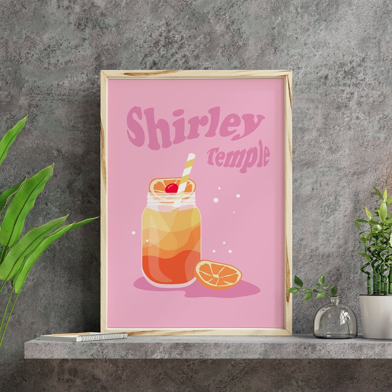 May include: A pink printable poster with the text "Shirley Temple" in a retro font. A mason jar filled with a layered orange and yellow drink with a maraschino cherry and a straw is pictured. A slice of orange is on the table next to the jar.
