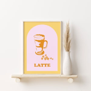 May include: A printable art print with a yellow background and a pink arch. Inside the arch is a stylized illustration of a latte in a glass with a brown and white design. The text "LATTE" is below the glass and there are brown coffee beans scattered around the glass.