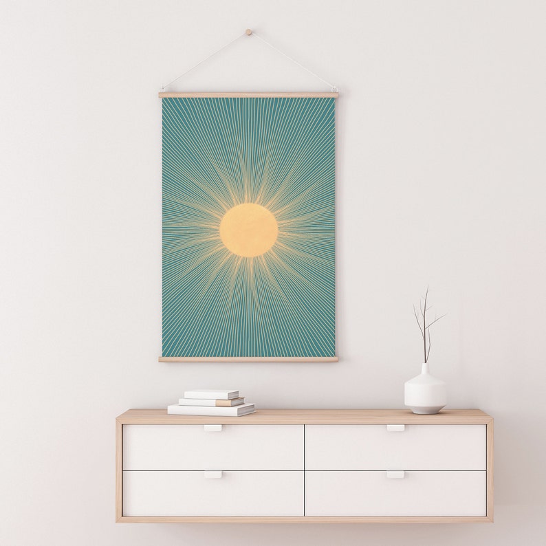 May include: A teal and yellow sunburst wall tapestry hanging on a white wall above a light wood dresser with white drawers.