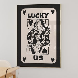 Pu&ograve; includere: Illustrazione in bianco e nero di una carta da gioco con una regina di picche. La carta dice "LUCKY US" in grassetto nero.