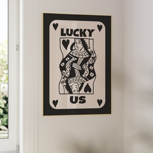 Pu&ograve; includere: Illustrazione in bianco e nero di una carta da gioco della regina di cuori con la parola "LUCKY" sopra la regina e la parola "US" sotto la regina.