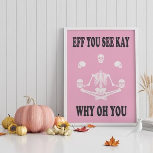 May include: A framed pink poster with white text and a skeleton illustration. The text reads "EFF YOU SEE KAY WHY OH YOU". The skeleton is in a seated yoga pose, holding skulls. Decorative pumpkins and fall leaves are in the foreground.