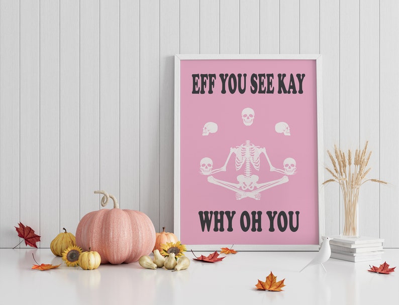 May include: A framed pink poster with white text and a skeleton illustration. The text reads "EFF YOU SEE KAY WHY OH YOU". The skeleton is in a seated yoga pose, holding skulls. Decorative pumpkins and fall leaves are in the foreground.