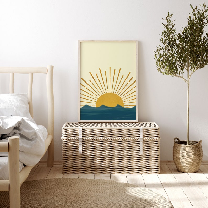 May include: A framed print of a minimalist sun and waves design. The sun is yellow with orange rays and the waves are blue. The background is a light yellow.