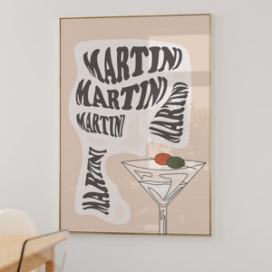 May include: A beige poster with a gold frame features a stylised illustration of a martini glass with olives and the word "MARTINI" repeated in a swirling pattern.
