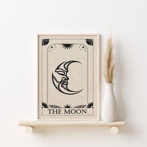 May include: A black and white illustration of the moon with a face on it. The moon is surrounded by stars and a sun. The text "THE MOON" is printed below the moon.