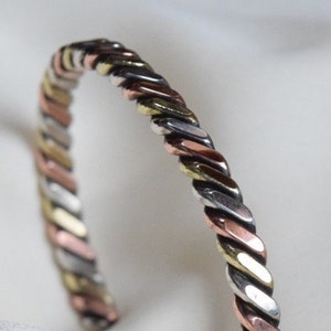 Peut inclure: Un bracelet jonc tressé en argent, cuivre et or. Le bracelet est composé de trois métaux différents qui sont entrelacés pour créer un design unique et élégant.