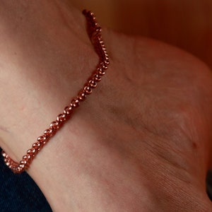 May include: A copper ankle bracelet with a chain-like design. The bracelet is made of small, round beads that are connected together.