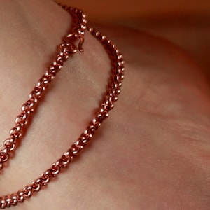 May include: A close-up of a copper chain bracelet on a person's wrist. The bracelet is made of two chains, one thicker than the other, and is a simple design.
