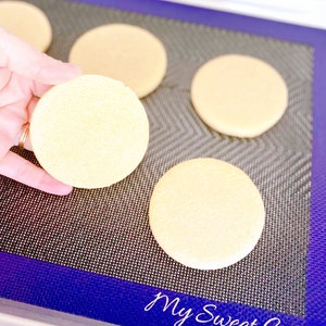May include: Four round, light yellow cookies on a blue and black silicone baking mat. The mat has the text "My Sweet Cuts" printed on it.