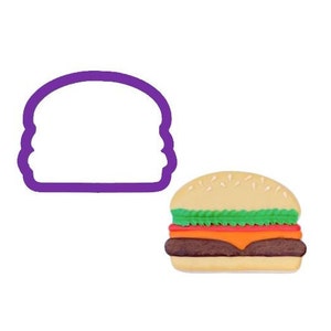 May include: A purple plastic burger-shaped cookie cutter next to a colorful, finished burger. The burger has a light brown bun sprinkled with seeds, green lettuce, a red tomato slice, orange cheese, and a dark brown patty.