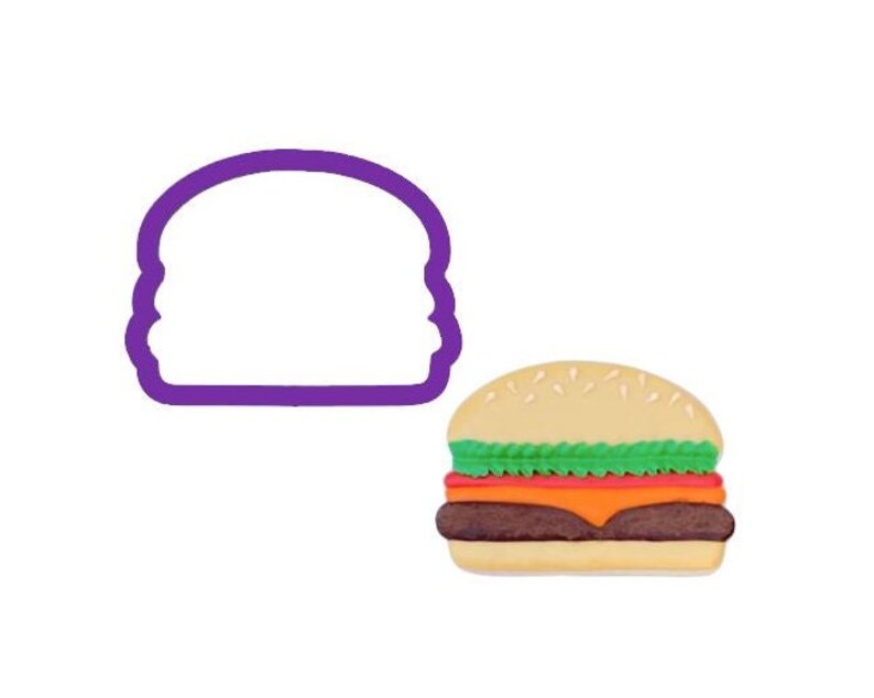 May include: A purple plastic burger-shaped cookie cutter next to a colorful, finished burger. The burger has a light brown bun sprinkled with seeds, green lettuce, a red tomato slice, orange cheese, and a dark brown patty.