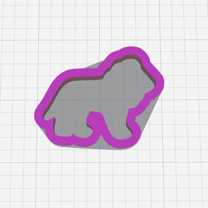 Puede incluir: Un cortador de galletas morado con forma de oso, que proyecta una sombra sobre una superficie gris. El contorno del cortador define la cabeza, el cuerpo y las patas del oso. El fondo es un patr&oacute;n de cuadr&iacute;cula blanca.