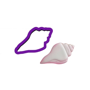 May include: Purple plastic seashell cookie cutter with a white seashell next to it.