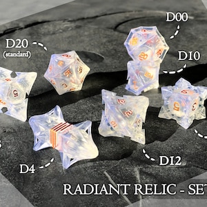 Op de afbeelding: Set van heldere, iriserende dobbelstenen met koperkleurige nummers. De set bevat een D4, een D6, een D8, een D10, een D12, een D20 en een D00. De dobbelstenen zijn gelabeld met de tekst "RADIANT RELIC - SET B".